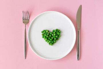 Top view of fresh green peas. Heart shaped green peas  in white platel on pink background. Space to write text font