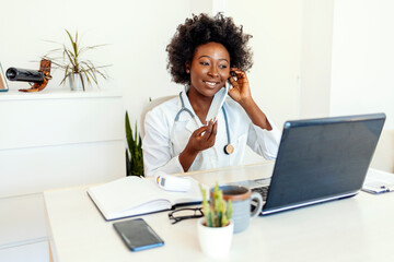 Portrait of a smiling young African American female doctor wearing a face mask while sitting at her...