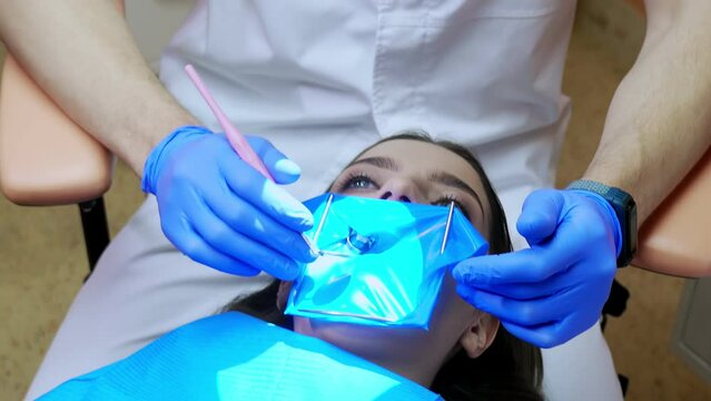 A dentist treats a woman's teeth using a cofferdam. Dental equipment.