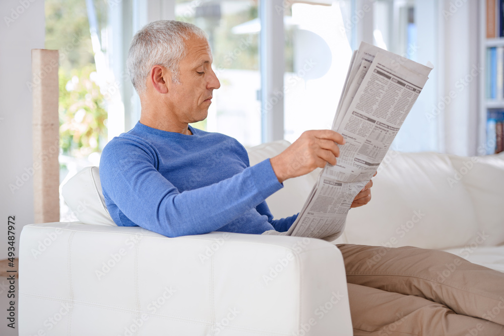 Poster Spending an easy saturday on the sofa. Shot of a mature man sitting on his living room sofa reading a newspaper.