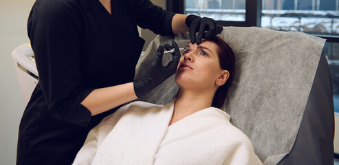Cosmetologist beautician aesthetician holding a syringe and making a beauty injection of botulinum toxin in the face of a middle aged woman in wellness spa clinic for rejuvenating anti-aging therapy