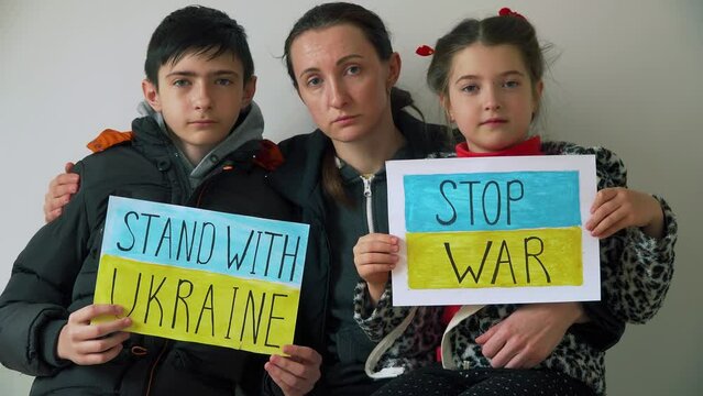 Woman and two children in refugee centre holding motivational packards with text Stop war and Stand with Ukraine against armored conflict. Crisis, peace, stop aggression in whole world