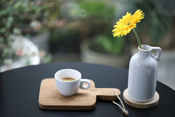 Coffee in a white cup with yellow gerbera flower on black wooden ntable