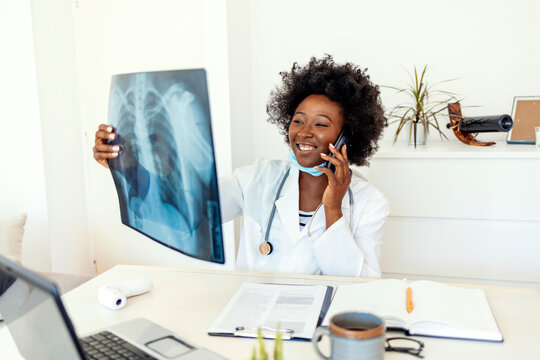 Doctor talks with patient about results while holding an x-ray in hands, a female doctor discusses the results with a patient or colleague via smartphone. Medicine, radiology and healthcare concept.