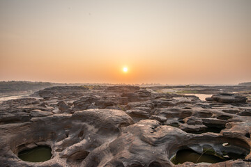 Obraz premium Sunrise at three thousand waved rocks under the natural sandstone group of the Mekong River that has been eroded for a long time in Ubon Ratchathani, Thailand.