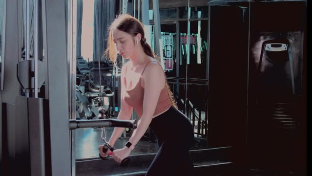 Woman doing fitness and strength training for the triceps on the cable in the fitness center. Asian fit girl doing warm up her triceps on the cable machine. Healthy lifestyle concept.