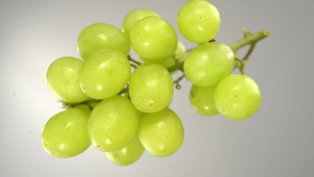 Green grapes fall on the glass surface, bottom view.