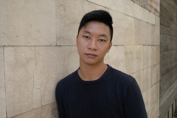 Fototapeta premium Portrait of young attractive asian man dressed in a dark T-shirt looking at camera outdoor.