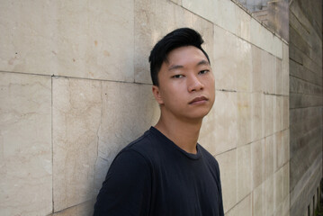 Portrait of young attractive asian man dressed in a dark T-shirt looking at camera outdoor.