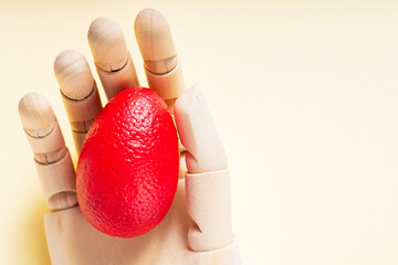 Red Easter egg in an artificial arm on a pastel yellow background. Surreal Easter concept. Top view. Copy space