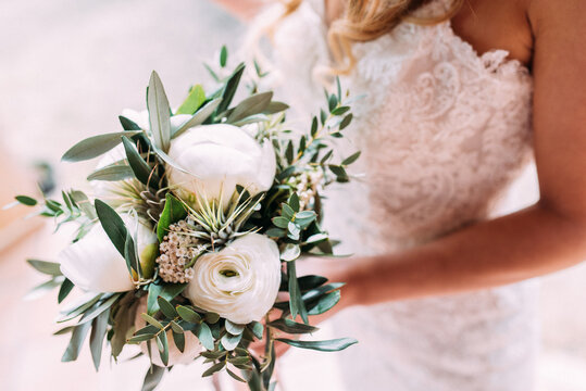 Wunderschöne Braut in weißem Spitzen Brautkleid hält Brautstrauss mit weissen Pfingstrosen horizontal