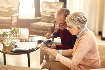 Making sure all our debts are in order. Shot of an elderly couple working out a budget while sitting on the living room sofa.