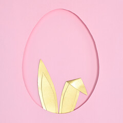 Egg shape frame with golden rabbit ears peek from hole on pastel pink background. Flat lay creative Easter concept