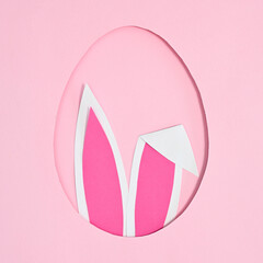 Egg shape frame with rabbit ears peek from hole on pastel pink background. Flat lay creative Easter concept