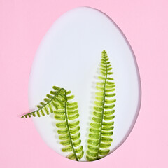 Easter creative concept. Egg shape with rabbit ears made of natural plants on pastel pink background. Flat lay