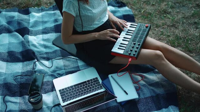 happy girl musician playing midi keyboard synthesizer and compose music outdoor