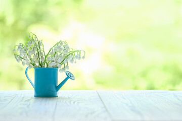 Lily of the valley flowers in mini watering can on white table, green abstract natural background....