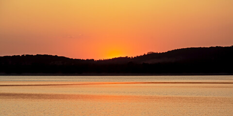 Orange glow after sunset over silhouette of mountains at Montargil lake, Portugal
