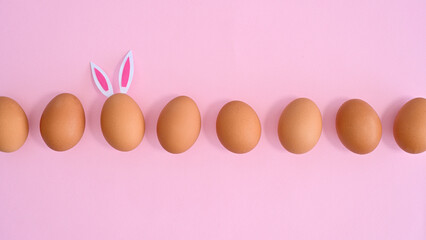 Easter pastel pink background with natural eggs and one different with bunny ears. Flat lay minimal. Spring holidays