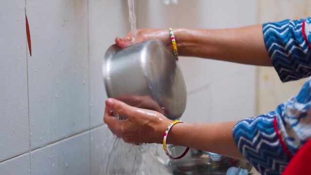 Close up of rural Indian woman's hands washing utensils in home. Making homework. Domestic life concept in India. Hands cleaning dish with flowing tap water. Cleaning concept