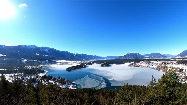 Panoramic view from a small hill in winter on Faak lake in Austrian Alps. Picturesque lake is surrounded by high mountains. The mountains are reflecting in calm surface of the lake. Taborhoehe, Tabor
