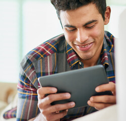 Checking his social media feeds. Shot of a handsome young man using his tablet while relaxing on the sofa at home.