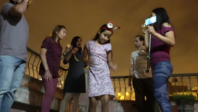 little girls dancing with their family on the rooftop toasting and taking photos on christmas night with glasses of champagne and having happy drinks among siblings, parents and grandparents