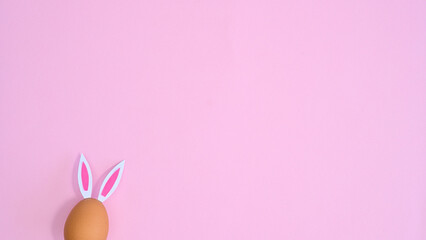 Natural egg with rabbit ears peek on pastel pink background with copy space. Easter flat lay minimal