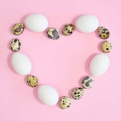 Creative copy space heart shape frame with white and quail natural eggs on pastel pink background. FLat lay