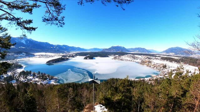Panoramic view from a small hill in winter on Faak lake in Austrian Alps. Picturesque lake is surrounded by high mountains. The mountains are reflecting in calm surface of the lake. Taborhoehe, Tabor
