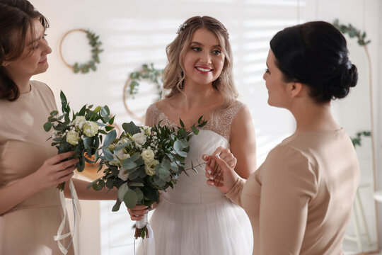 Happy bride and her bridesmaids with beautiful bouquets at home