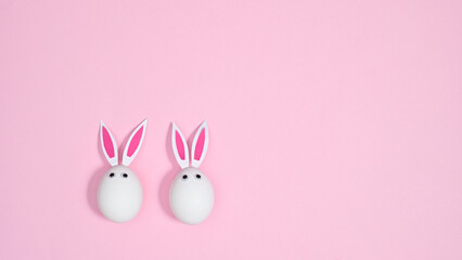 White eggs with rabbit ears on pastel pink background. Flat lay minimal creative concept. Easter holidays
