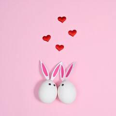 White eggs with rabbit ears in love with romantic red hearts on pastel pink background. Flat lay minimal creative concept. Easter holidays