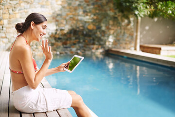 My tablet goes everywhere with me. Shot of a young woman relaxing by the pool with her tablet.