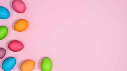 Vibrant pastel pink background with copy space and colorful Easter eggs. Flat lay creative minimal concept.