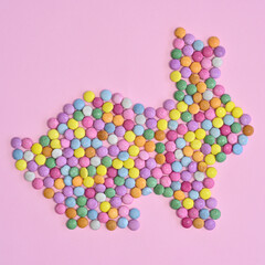 Creative rabbit bunny made with colorful candies on pastel pink background. Flat lay Easter concept