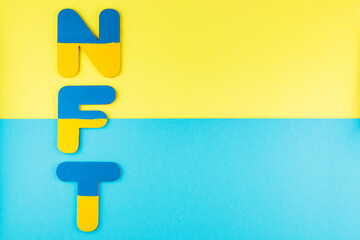 Fototapeta premium NFT inscription on a blue-yellow background. Non-fungible token in colors of Ukrainian flag. Ukrainian crypto art concept. Top view. Copy space