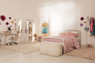 Stylish teenager's room interior with computer, comfortable bed and painting easel