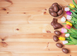 Chocolate Easter eggs, chocolate bunny and colorful tulip flowers as border on wooden background.
