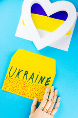 White heart on a blue-yellow background. Artificial hand holds an envelope with the inscription Ukraine . Concept of peace, love and support of Ukraine