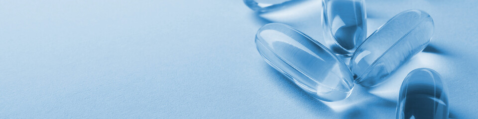 Fish oil softgels. Vitamins and healthy lifestyle. Blue tinted banner or headline. Softgel closeup....