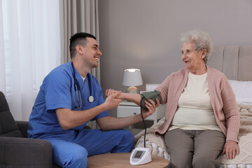 Young caregiver measuring blood pressure of senior woman in bedroom. Home health care service