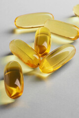Fish oil. Yellow softgels or capsules lie on white or light gray surface. Vertical illustration about vitamins and healthy lifestyle. Softgel closeup. Omega-3 fatty acids. Macro