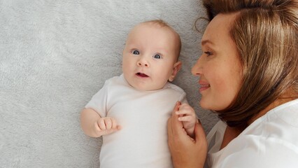 Happy newborn baby with his mother. Healthy newborn baby in a white t-shirt with mom. Closeup Faces of the mother and infant baby. Cute Infant boy and parent, top view. Happy family portrait