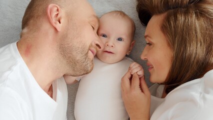 Happy parents with his newborn baby, top view. Happy family. Healthy newborn baby with mom and dad. Close up Faces of the mother, father and infant baby. Cute Infant boy and parents.