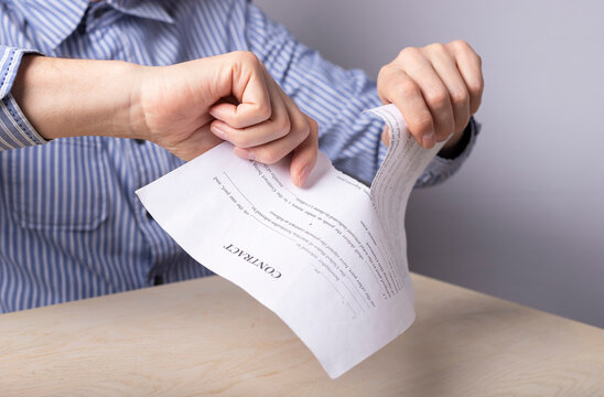 Man hands closeup tearing contract. Termination of partnership, deal concept. Man sitting at desk in office and tearing document. Worker firing. High quality photo