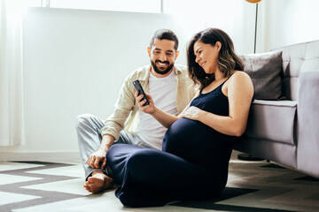 Pregnancy and technology concept. Pregnant woman and her husband spending time together using...