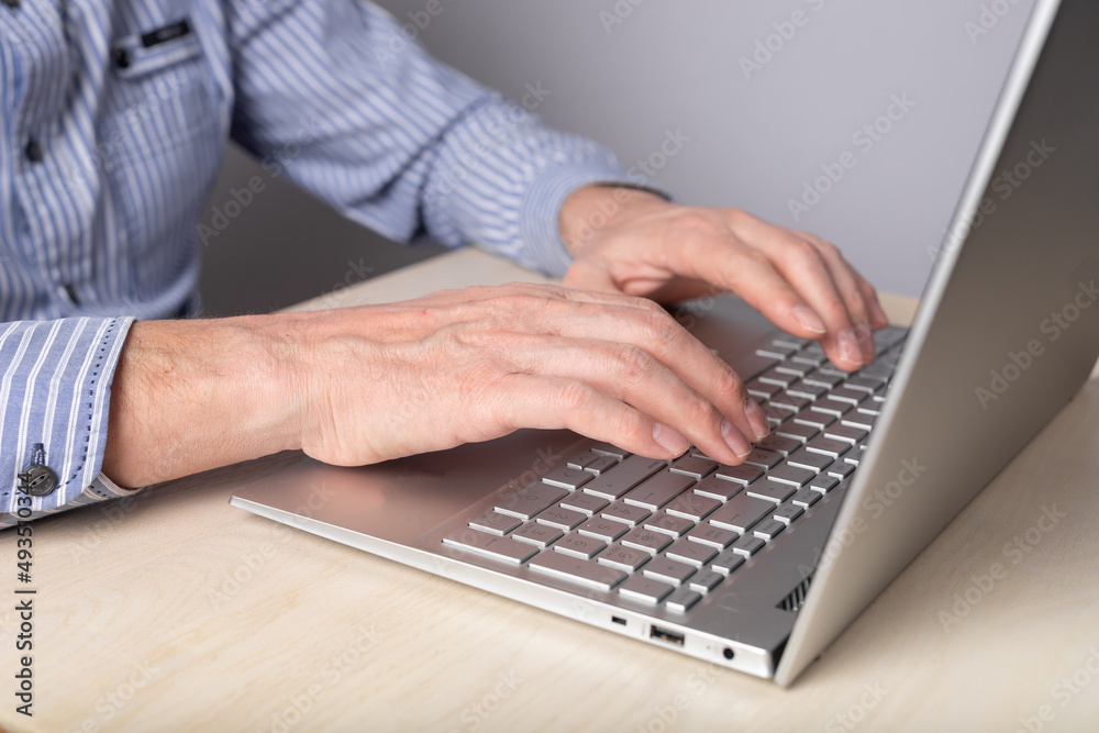 Fototapete Man hands closeup typing on laptop keyboard. Man sitting at table with computer and working remotely, studying online, surfing Internet. High quality photo