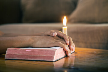 Hands praying on bible with candle light in at home