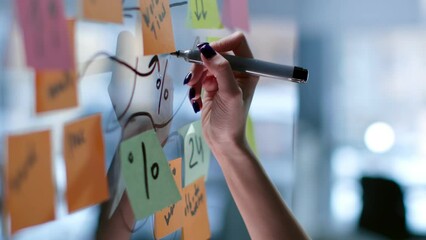 Cropped shot of female hand writing on glass board with colorful sticky notes